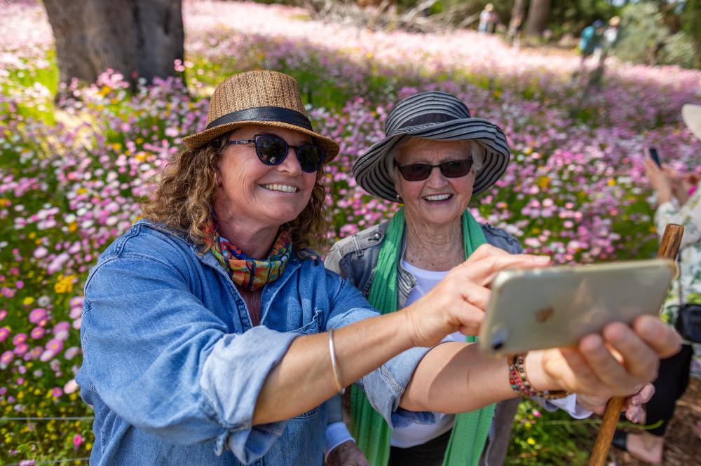 Two women taking photos in front of the Everlasting garden bed.